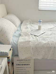 an unmade bed with white sheets and blue polka dots on it, next to a stack of books