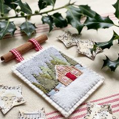 an embroidered christmas ornament on a table with holly leaves and other decorations around it