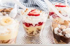 four desserts in plastic cups with spoons on a tray, including bananas and strawberries