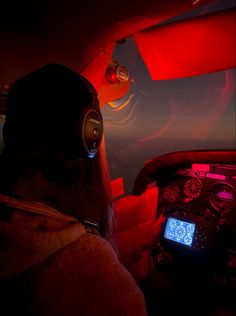 a person wearing headphones sitting in an airplane cockpit at night with the lights on