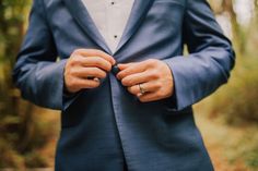 a man in a blue suit and white shirt is tying his wedding ring on his lapel