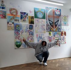 a person kneeling down in front of a wall with many pictures on it and arms spread out