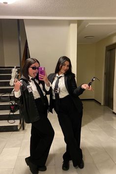 two women dressed in black and white taking pictures with their cell phones while standing next to each other