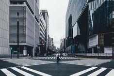 a person walking across a cross walk in the middle of a city with tall buildings