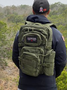 a man with a backpack on his back looks out over the trees and brush in the distance