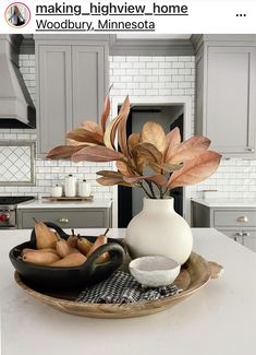 a white vase filled with flowers sitting on top of a wooden plate next to a bowl