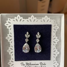 a pair of diamond earrings is displayed in a white box with lace border around it