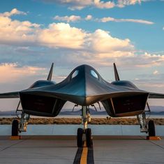 a fighter jet sitting on top of an airport tarmac under a cloudy blue sky