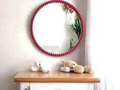 a round mirror sitting on top of a dresser next to a teddy bear