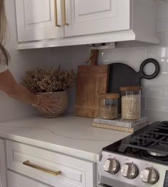 a woman is reaching for some food in a bowl on the kitchen counter next to an oven