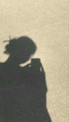 the shadow of a person holding a skateboard in their hand and wearing a hat