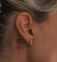 a woman's ear has a small rose tattoo on it