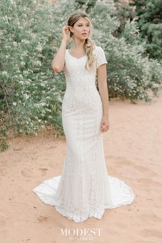 a woman standing in the sand wearing a white wedding dress and holding her hand to her ear