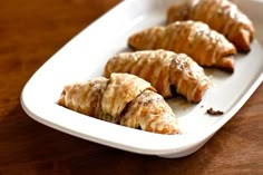 three croissants on a white plate sitting on a wooden table