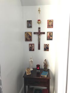 a small wooden table in front of a wall with pictures and a crucifix on it