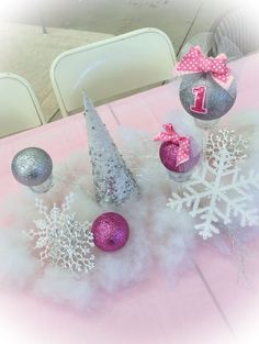 a table topped with ornaments and snowflakes on top of a pink table cloth