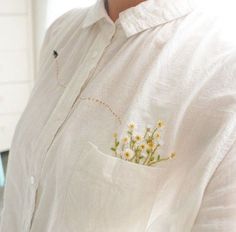 a woman wearing a white shirt with yellow flowers in the pocket