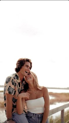 a man and woman sitting next to each other on a wooden bench near the ocean