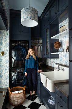 a woman standing next to a kitchen sink in front of a washer and dryer