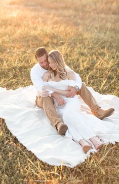 a man and woman sitting on top of a blanket in the middle of a field