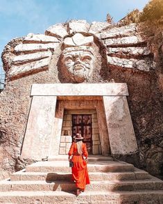 a woman in an orange dress is walking up some steps to a large carved head