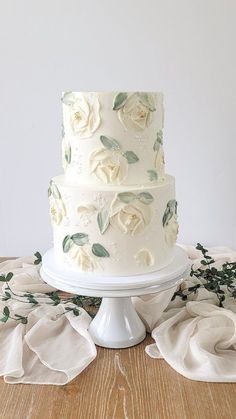 a three tiered white wedding cake with flowers on the side and greenery around it