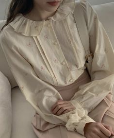 a woman sitting on top of a couch wearing a white shirt and pink pants with ruffles