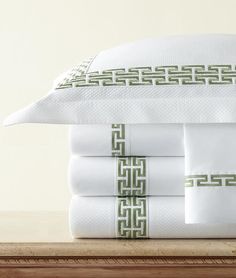 a stack of white sheets and pillows with green trimmings sitting on top of a wooden table