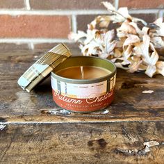 a small tin candle sitting on top of a wooden table next to some dried flowers