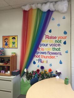 a room with a rainbow curtain and flowers on the wall, next to a desk