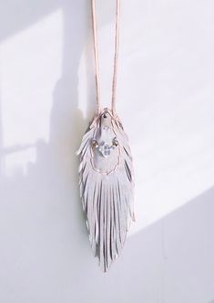 a white necklace with a feather pendant hanging from it's side