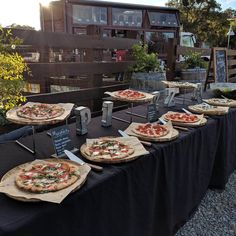 several pizzas sitting on top of wooden trays lined up on a long table