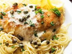 a white plate topped with pasta and meat next to lemon wedges on a wooden table