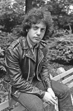 a black and white photo of a man in a leather jacket sitting on a bench