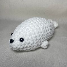 a crocheted white stuffed animal with black eyes on a gray background, looking at the camera