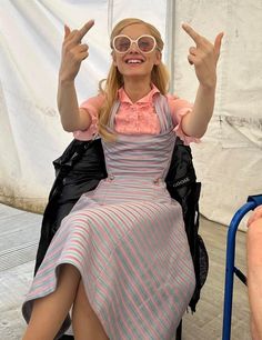 a woman sitting in a chair with her hands up to the side and wearing glasses