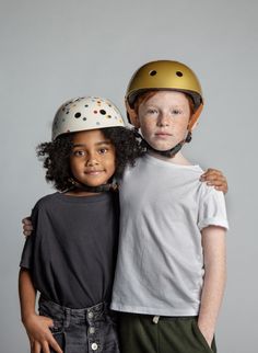 two children with helmets on their heads posing for a photo in front of a gray background