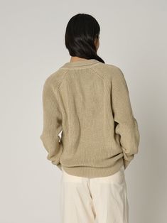 the back view of a woman wearing a beige sweater and white pants, looking down at her