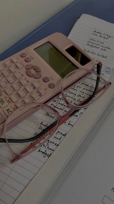 a pink calculator sitting on top of an open notebook next to eyeglasses