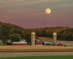 the full moon is setting over an old farm and silos in rural countrysides