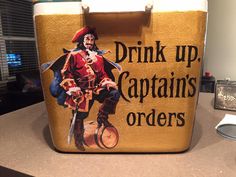 a cooler sitting on top of a counter next to a cup and bottle opener with an advertisement for drink up captain's orders