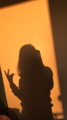 the shadow of a woman holding her hand up in front of an orange wall with light coming through it