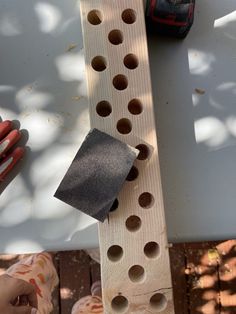 a piece of wood with holes in it and someone's hand next to it