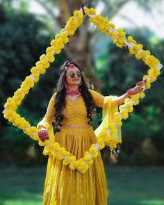 a woman in a yellow dress with flowers on her head and arms, holding a flower arch