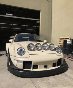 a white sports car parked in front of a garage with its hood up and lights on