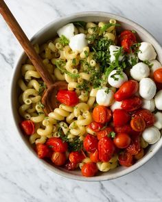 a bowl filled with pasta and tomatoes on top of a marble countertop next to a wooden spoon