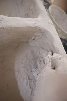 a close up of some white clay with one hand on the edge and another in the background