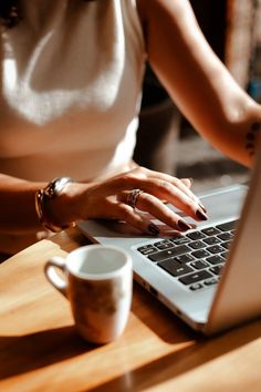 a woman is typing on her laptop at a table with a coffee cup and mug