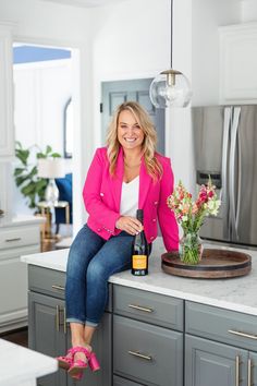 a woman sitting on top of a kitchen counter with a bottle of wine in her hand