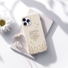 an iphone case sitting on top of a white envelope next to a flower and a daisy